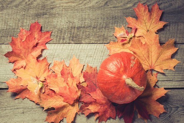 Orange pumpkin and maple leaves on wooden board. Fall pattern.