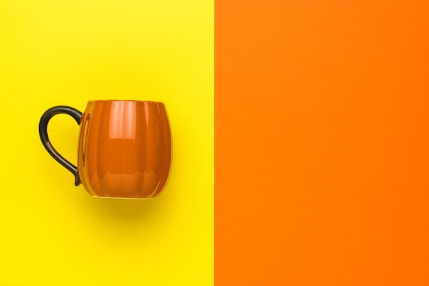 Photo orange pumpkin-shaped mug on a yellow and orange background. pumpkin style.