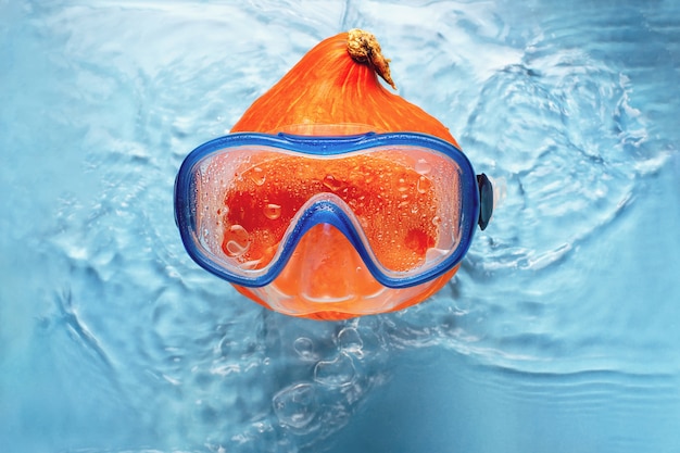 Photo orange pumpkin swimmer in a mask in blue water halloween concept