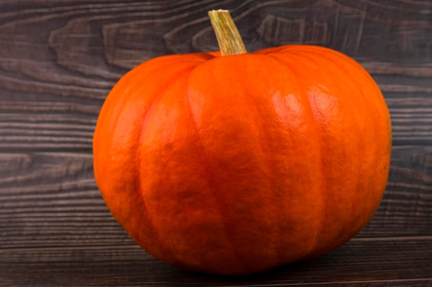 Orange pumpkin with a stem closeup on a plank wooden background Autumn background Copy space