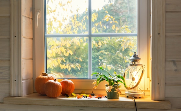 Orange pumpkins on windowsill, candles, autumn leaves, lantern.