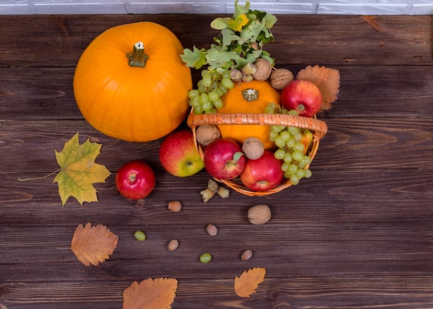 Orange pumpkins with apples and pears in a basket with grapes nuts and leaves on a brown wooden table View from above Harvest concept