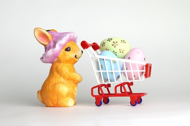 An orange rabbit with a shopping cart decorated eggs in a cart Buying eggs for Easter