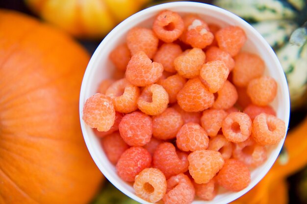 Orange raspberry in a white bowl on the background of autumn decorative pumpkins Autumn berries concept