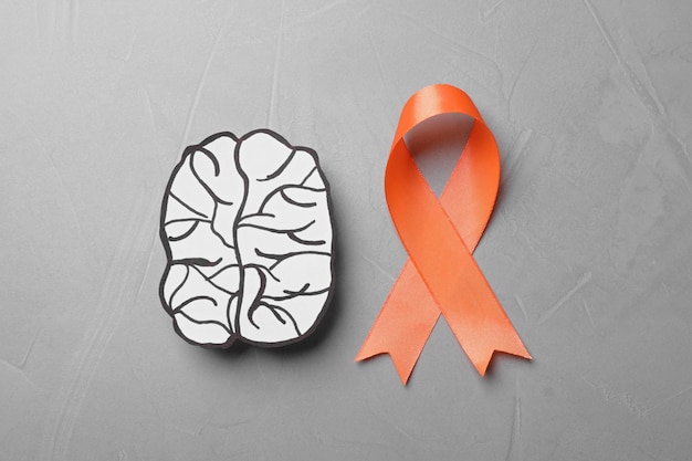 Orange ribbon and paper brain cutout on light grey table flat lay Multiple sclerosis awareness