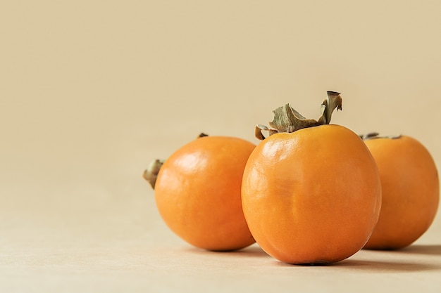 写真 パステルベージュの背景にオレンジ色の熟した柿。