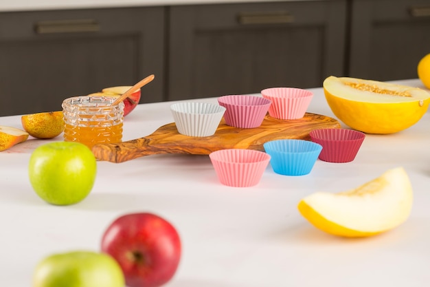 オレンジ色の丸いシリコーン カップケーキ グラタン皿の多くは、果物の横にある木製のまな板の上に横たわり、