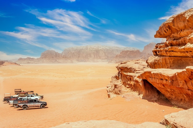 Orange sands and rocks of Wadi Rum desert with cars in the foreground Jordan