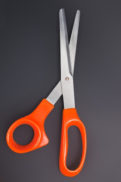 Orange scissors on the black background