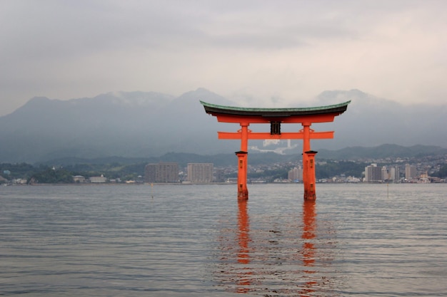 Orange shrine in river against mountains during foggy weather