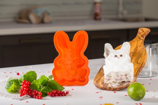 Orange silicone mold rabbit for baking cakes, standing behind a man and hands, next to fruits and