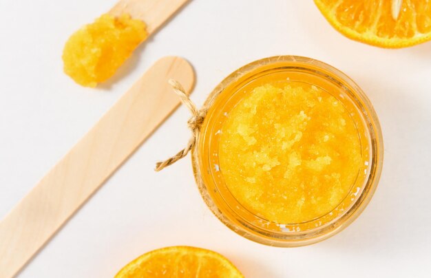 Orange skin cleanser in a glass container on a white table top view Sugar and citrus scrub closeup