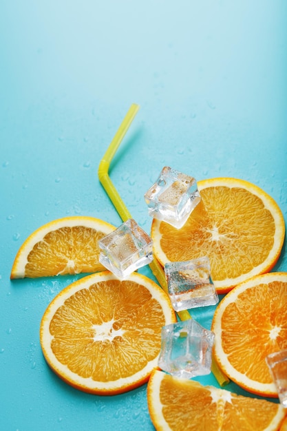 Дольки апельсина и кубики льда с трубочкой на синем фоне в форме коктейля. Концепция напитка «Лимонад» - это летняя освежающая композиция. Вид сверху
