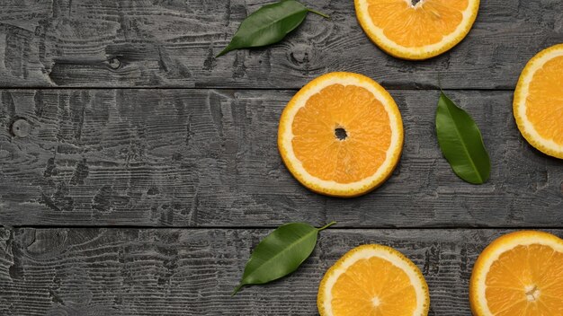 Orange slices with leaves on a wooden background. Space for the text. A popular tropical fruit. Flat lay.