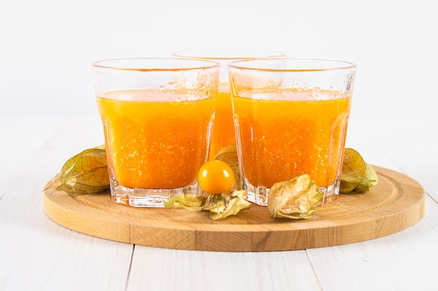 An orange smoothie made of physalis on a white wooden table.