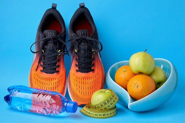 青い背景に巻尺と果物のリンゴとオレンジを測定するオレンジ色のスニーカー