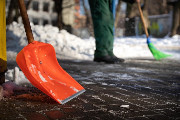 An orange snow shovel in the foreground and in the second a worker is sweeping the sidewalk out of