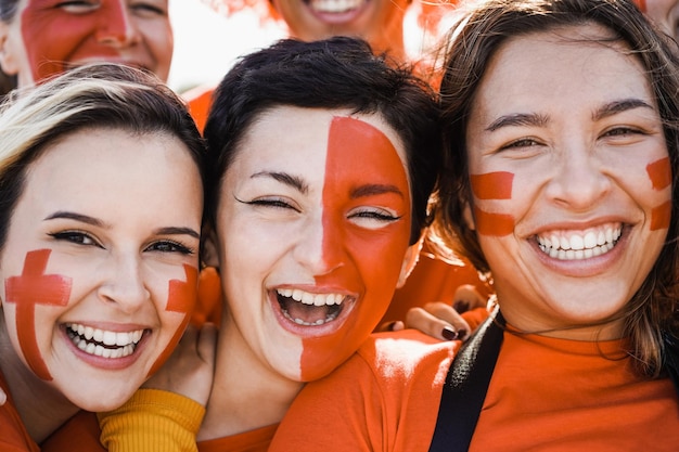 Orange sport fans having fun supporting their team Football supporters having fun at competition event Focus on left girl eye