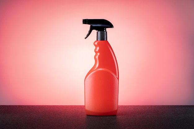 ピンクの背景にクリーニング製品のオレンジ色のスプレーボトル