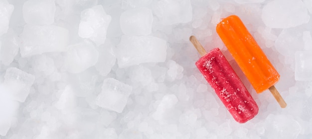 Orange and strawberry popsicles on ice cubes panorama view