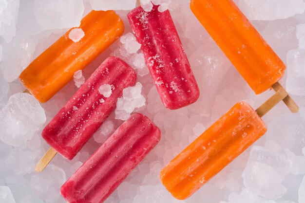 Orange and strawberry popsicles on ice cubes, top view
