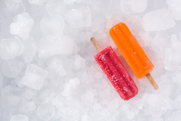 Orange and strawberry popsicles on ice cubes,, top view