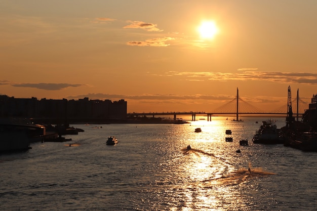 Orange sunset over the river with a big bridge and boats