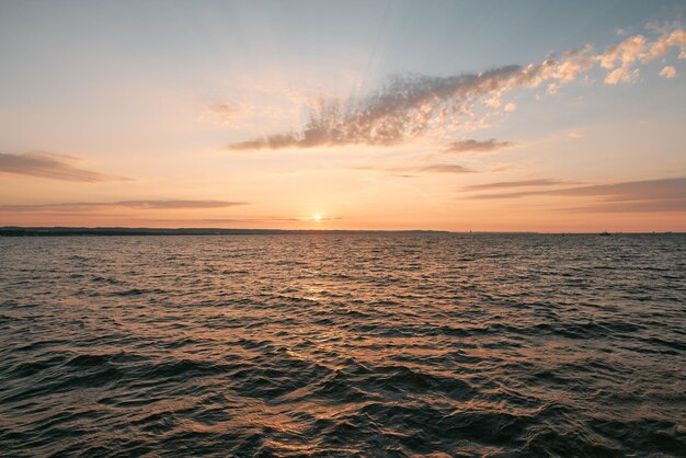 焦点が合っていない大きな小石の岩と海岸のオレンジ色の夕日海の太陽の反射の前にぼやけた石