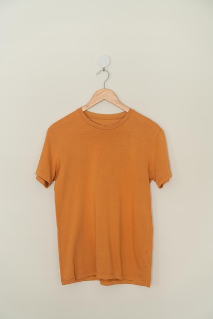 orange t-shirt hanging with wood hanger on wall