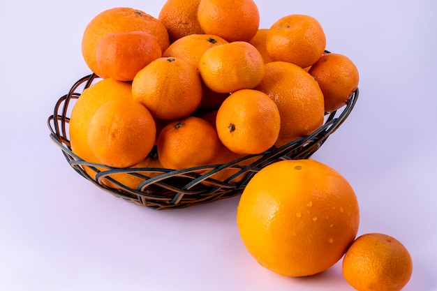 白いテーブルの上の籐のバスケットにオレンジとみかん。