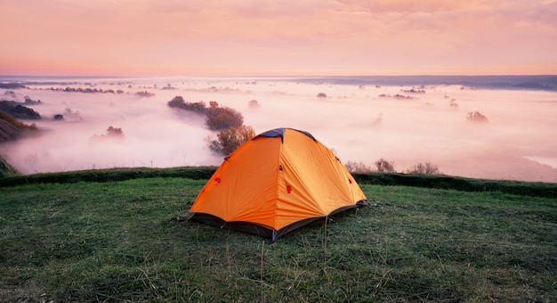 Tenda arancione sulla collina sopra il fiume nebbioso