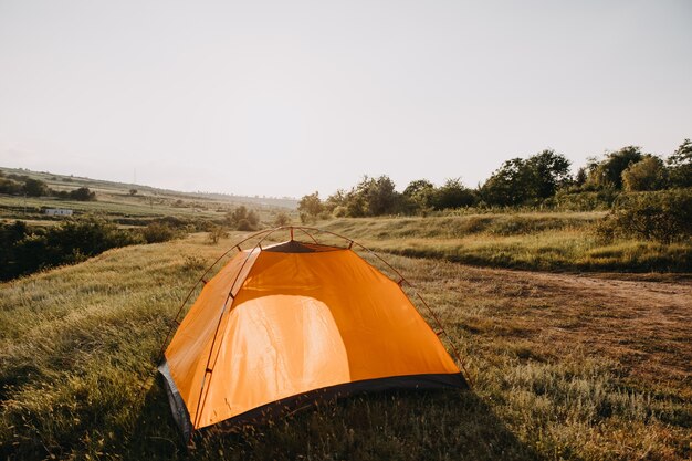 An orange tent on a meadow in mountains.