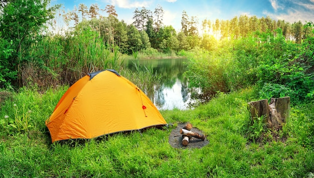 Tenda arancione sulla riva del fiume tra erba verde e alberi. giorno soleggiato