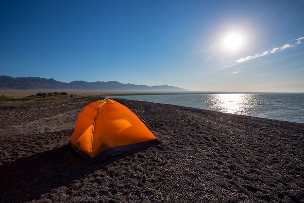 Orange tourist tent in the lake shore under the dramatic sunset sky