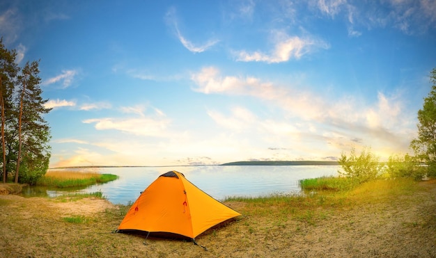 Оранжевая туристическая палатка на берегу реки в солнечный день Панорама высокого разрешения