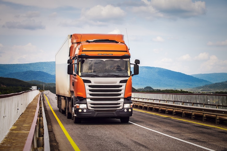 Photo orange truck on a road moving by a bridge