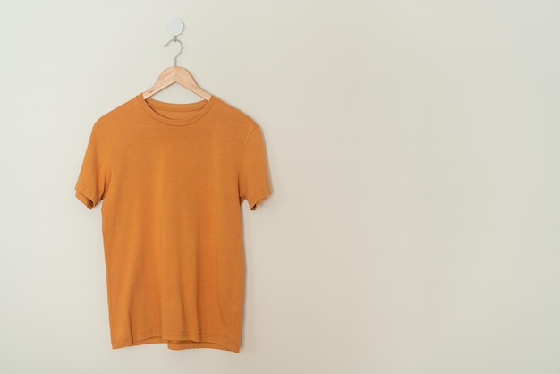 Orange tshirt hanging with wood hanger on wall