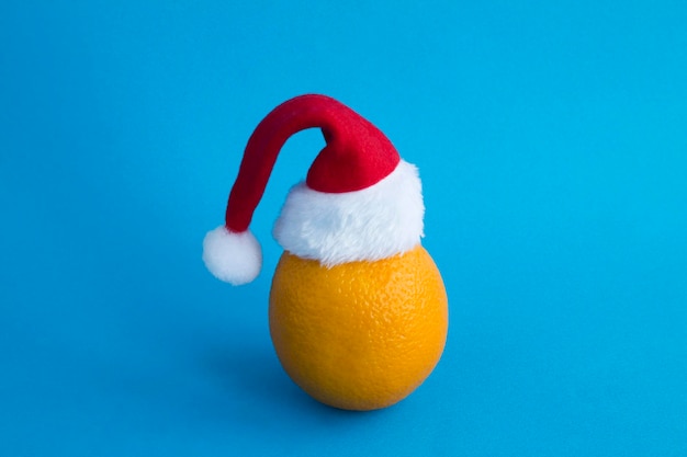 Orange with Santa Claus hat on the blue background Christmas composition Closeup Copy space