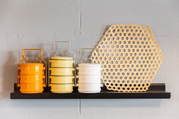 Orange, yellow and white steel food carrier of tiffin on wooden shelf. Thai style served portion size. Restaurant Decoration.