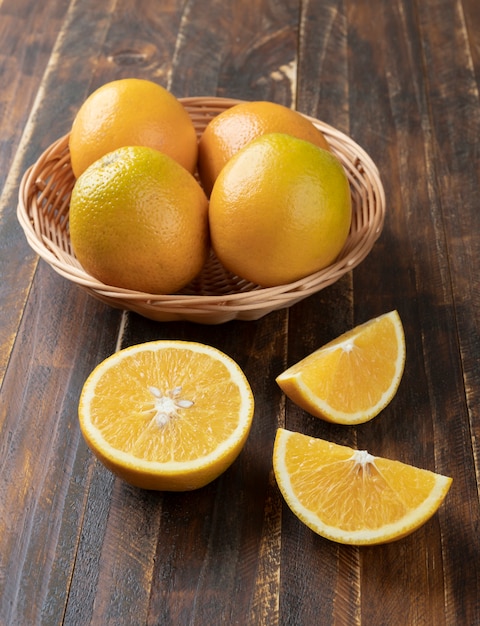 Апельсины в корзине с разрезанными фруктами над деревянным столом.