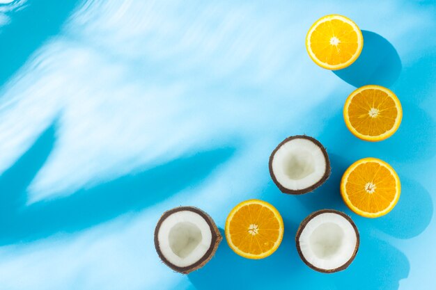 Oranges and coconut on a blue surface under natural light with shadows. Flat lay, top view.