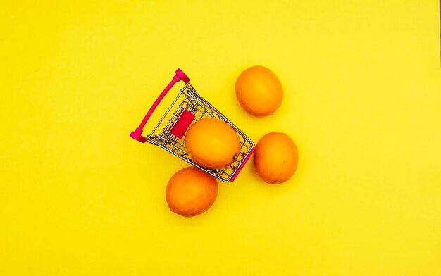 Oranges in an iron grocery cart on a yellow background business and healthy food concepts