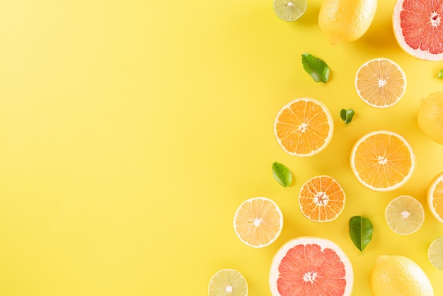 Oranges, lemon and green leaves on pastel yellow paper, copy space.