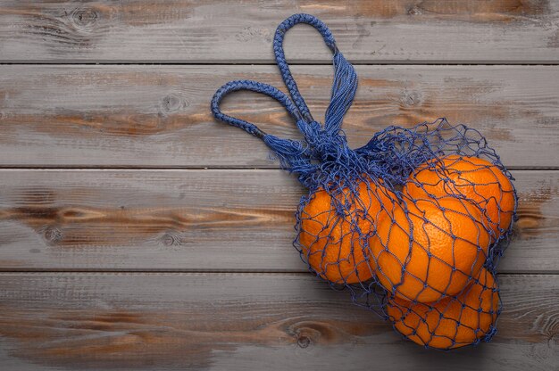 Oranges in a mesh string bag made of natural material on wood surface 