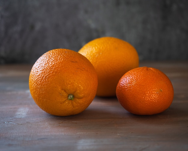 Oranges and one tangerine lie on a roughly painted table Closeup of three ripe fruits