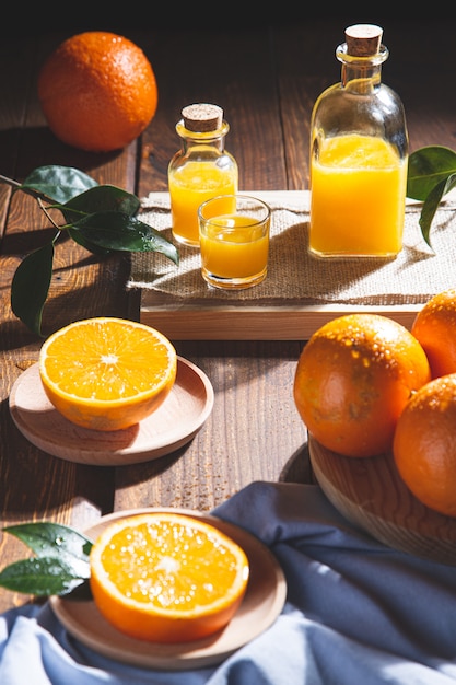 Oranges, oranges slices, orange leaves, and glass containers with orange juice on wooden table.