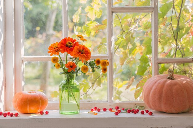 Oranje bloemen met pompoenen op wit venster