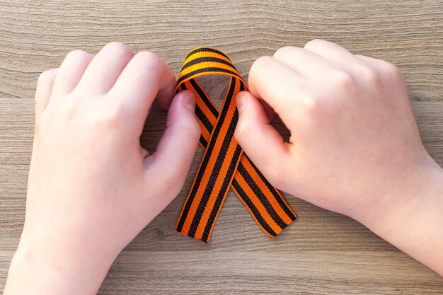 Oranje en zwart gestreept lintsymbool op 9 mei in handen die op witte muur worden geïsoleerd. Dag van de Overwinning