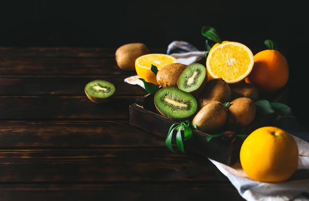 Oranje fruit en kiwi's in een houten krat, evenals gesneden op een houten tafel.