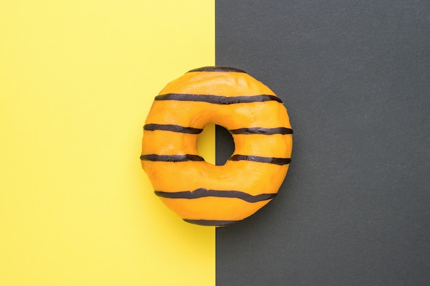 Oranje geglazuurde donut op de grens van gele en zwarte kleuren. Een populaire zoete snack.